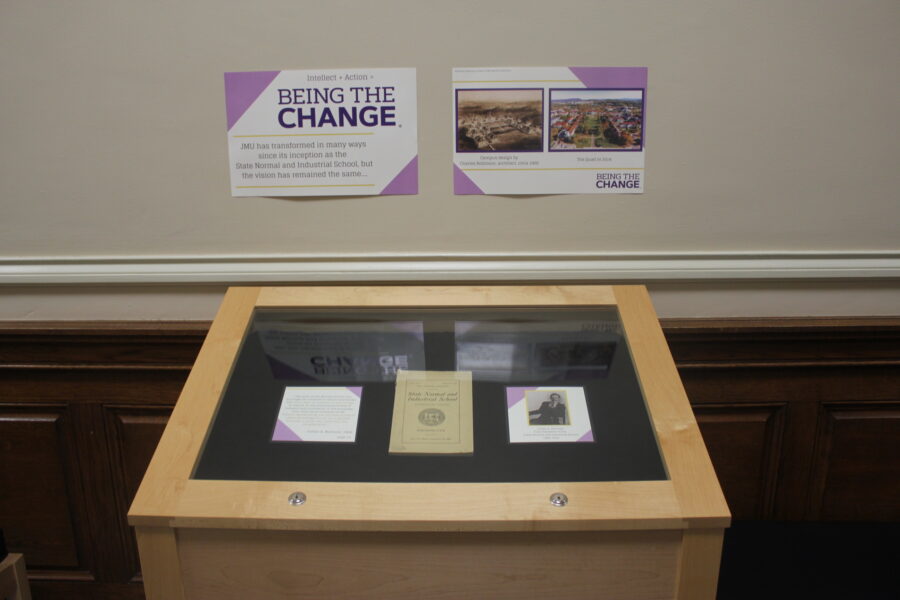 A glass-topped display table contains several documents related to the Being the Change exhibit.