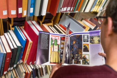 A view over the back shoulder of someone looking at a graphic novel in the library stacks.
