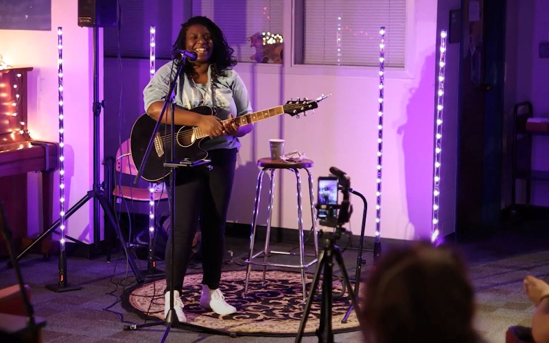 A musician holding a guitar stands behind a microphone
