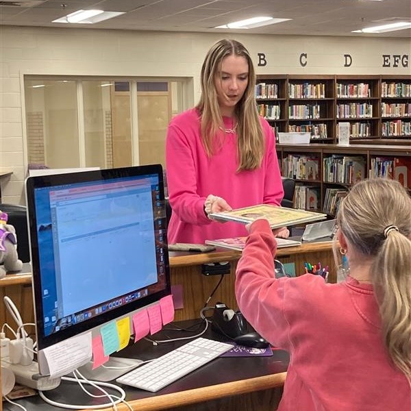 photo of a student picking up a children's book from a student employee at the ETMC service desk