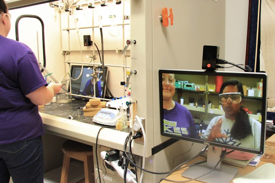 Hearing-impaired students use a computer monitor installed inside a fume hood to communicate with sign language interpreters while performing a chemistry experiment. 