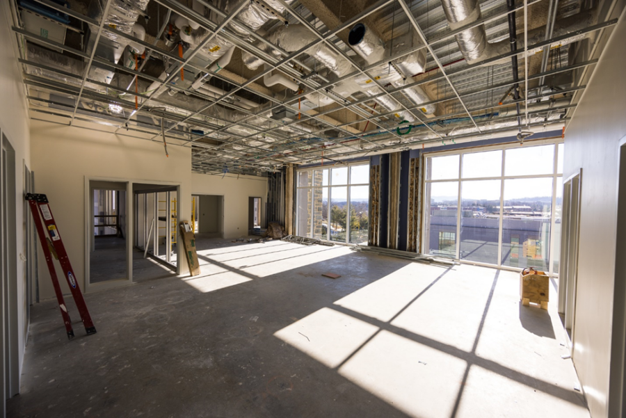 Sun streaming through large windows casts shadows on the floor of office space under construction with visible mechanical systems