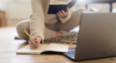 person sitting on floor using a laptop, book, pencil and paper