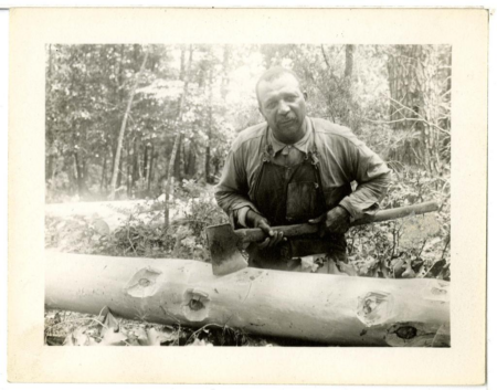 black and white photo of a man standing over a log holding an ax