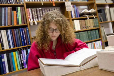 a person looking at a book in jmu special collections with books on shelves behind them